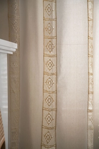 Detailed view of hollow crochet stripes on beige linen curtain with tassels