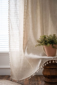 Close-up of linen curtain with decorative hollow lace stitching and cotton ball tassels