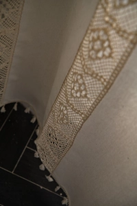 Detailed close-up of beige linen curtain with intricate crochet lace and tassel trim