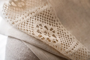 Macro detail of beige polyester-linen curtain featuring delicate hollow-out lace and fringe