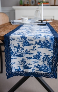 Chemin de table bleu Toile de Jouy détaillé avec bordures en dentelle sur bois sombre
