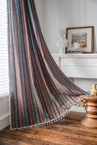 Détail d'un rideau bohème rayé en coton et lin avec des pompons blancs et des motifs colorés
