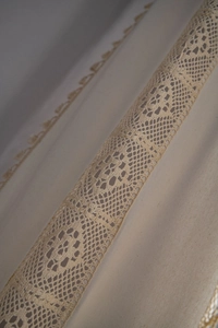 Detailed close-up of cream curtain with hollow lace trim and natural fabric texture