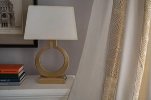 Modern gold ring base table lamp with white fabric shade in a cozy home setting decor