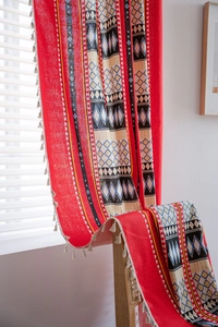 Detail view of red bohemian curtain fabric with geometric patterns and beige pompom tassels