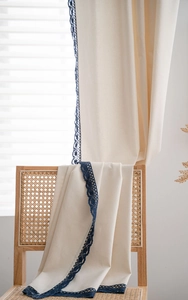 Detail of off-white linen texture curtain with blue crochet lace on a rattan chair