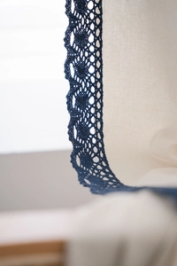 Detail of navy blue crochet lace trim stitched on off-white linen fabric curtain