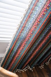 Détail d'un rideau de style bohème à rayures géométriques colorées et finitions de franges blanches