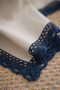 Detailed close-up of cream white fabric with dark blue crochet lace edge and linen texture