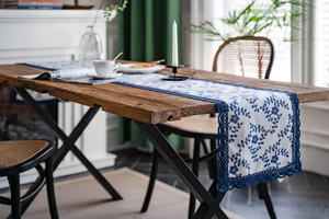 Detail of blue floral embroidery and navy lace edge on a rustic cotton linen table runner