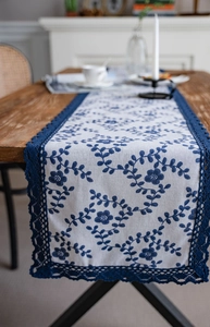 Detailed close-up of navy blue floral embroidery and crochet lace on cream table runner