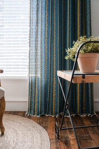 Detail of bohemian striped curtains featuring blue prints and white fringe tassels