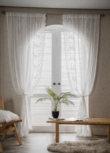 Detailed view of white floral lace curtains on a white arch window with soft lighting