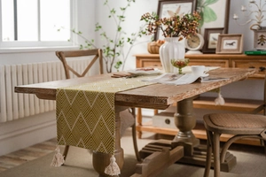 Close-up of yellow geometric herringbone table runner with elegant white tassels on wood