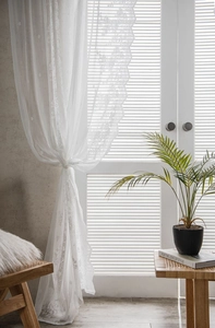 Detail of white lace curtains with scalloped edges and delicate floral semi-sheer patterns