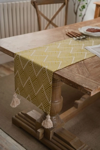 Detail of yellow geometric jacquard table runner with cotton tassels on wood table