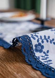 Close-up of blue floral print table runner with intricate navy crochet lace trim