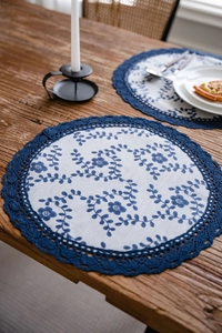 Close-up of circular floral placemat with blue crochet lace on a dark wooden table