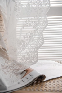 Detailed macro of white lace curtain with elegant floral embroidery and scalloped edges