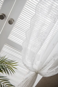 Detailed close-up of vintage white lace curtains with floral patterns and scalloped edges