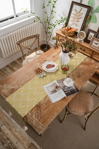 Detail of yellow geometric jacquard table runner with decorative cream tassels