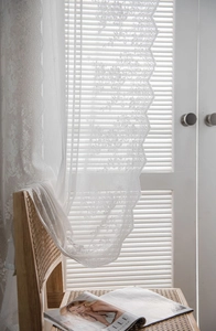 Detail of white vintage floral lace curtain with elegant scalloped edges and sheer texture