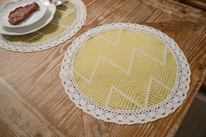 Detail of round yellow geometric table mat with elegant white crochet lace border