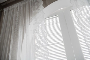 Close-up of white lace curtain with delicate floral embroidery and wavy scalloped edges