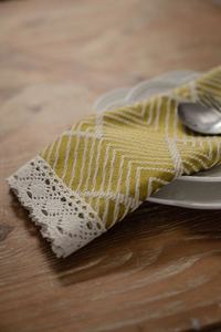 Detail of mustard yellow geometric table runner with white lace edges on a wooden table
