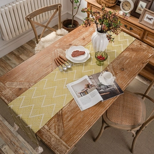 Nordic yellow table runner with geometric jacquard pattern and white tassels on wood table