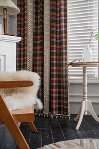 Detailed close-up of red and brown plaid curtains with beige crochet lace and tassel fringe