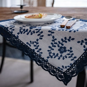 Floral embroidered table runner with navy blue lace edge on a rustic wooden dining table