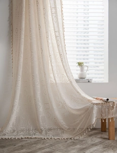 Gros plan du rideau en dentelle crochet beige avec motif ajouré et pompons bohèmes