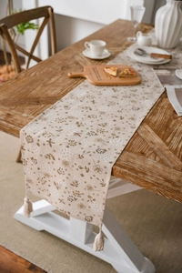 Dettaglio del runner da tavola in cotone beige con stampa a dente di leone e nappe