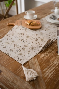 Dettaglio del runner da tavola rustico con stampa floreale marrone e nappe bianche