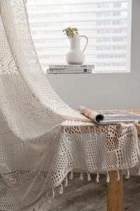 Gros plan du rideau au crochet crème avec motifs géométriques et bordures à franges