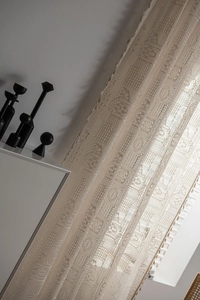 Détail du rideau au crochet beige avec motifs géométriques et bord à franges