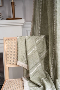 Detail of green woven curtain featuring white leaf embroidery and cream fringe tassels