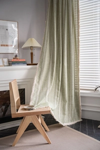 Close-up of sage green linen textured curtain with vertical weaving and ivory fringe detail
