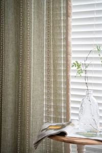 Detail of green textured linen curtain with vertical stripes and delicate fringe edges