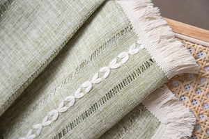 Close-up of green linen table runner featuring leaf embroidery and beige fringe tassels