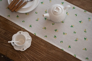 Detail of lemon print table runner on wooden desk with tea set and cotton linen texture