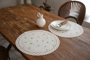 Detail of round cotton linen placemat with yellow flower prints and lace edge on wood table