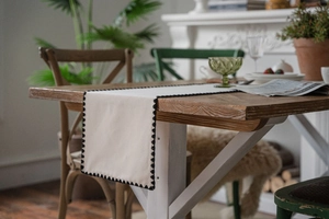 Detail of cream table runner with black scalloped embroidery on a rustic wooden table