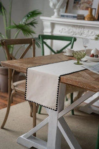 Detail showing cream table runner with black triangle embroidery on solid wood table