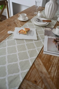 Detailed view of sage green Moroccan trellis table runner on a solid wood dining table