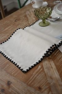 Close-up of beige linen table runner featuring elegant black scalloped crochet edges