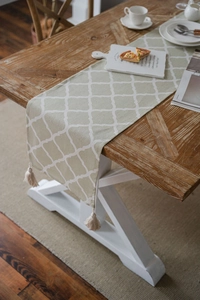 Detail of sage green table runner with white Moroccan patterns and beige tassels