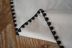 Close-up of white linen runner with black triangle embroidery on rustic wood table