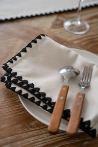 Detail of cream fabric table runner with intricate black scalloped embroidered edges